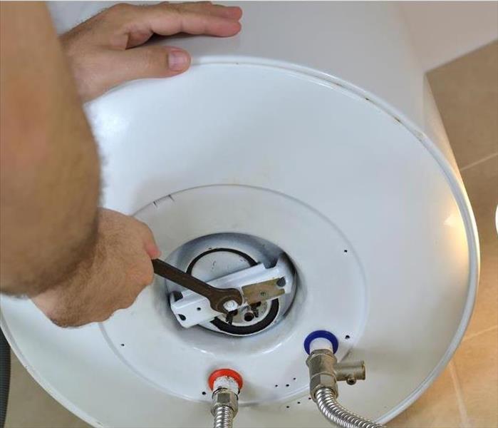Man's hands unscrewing a screw-nut on a water heater with a wrench on a boiler