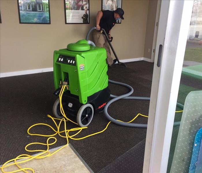 A man using a water extraction vacuum on a carpet of a building 